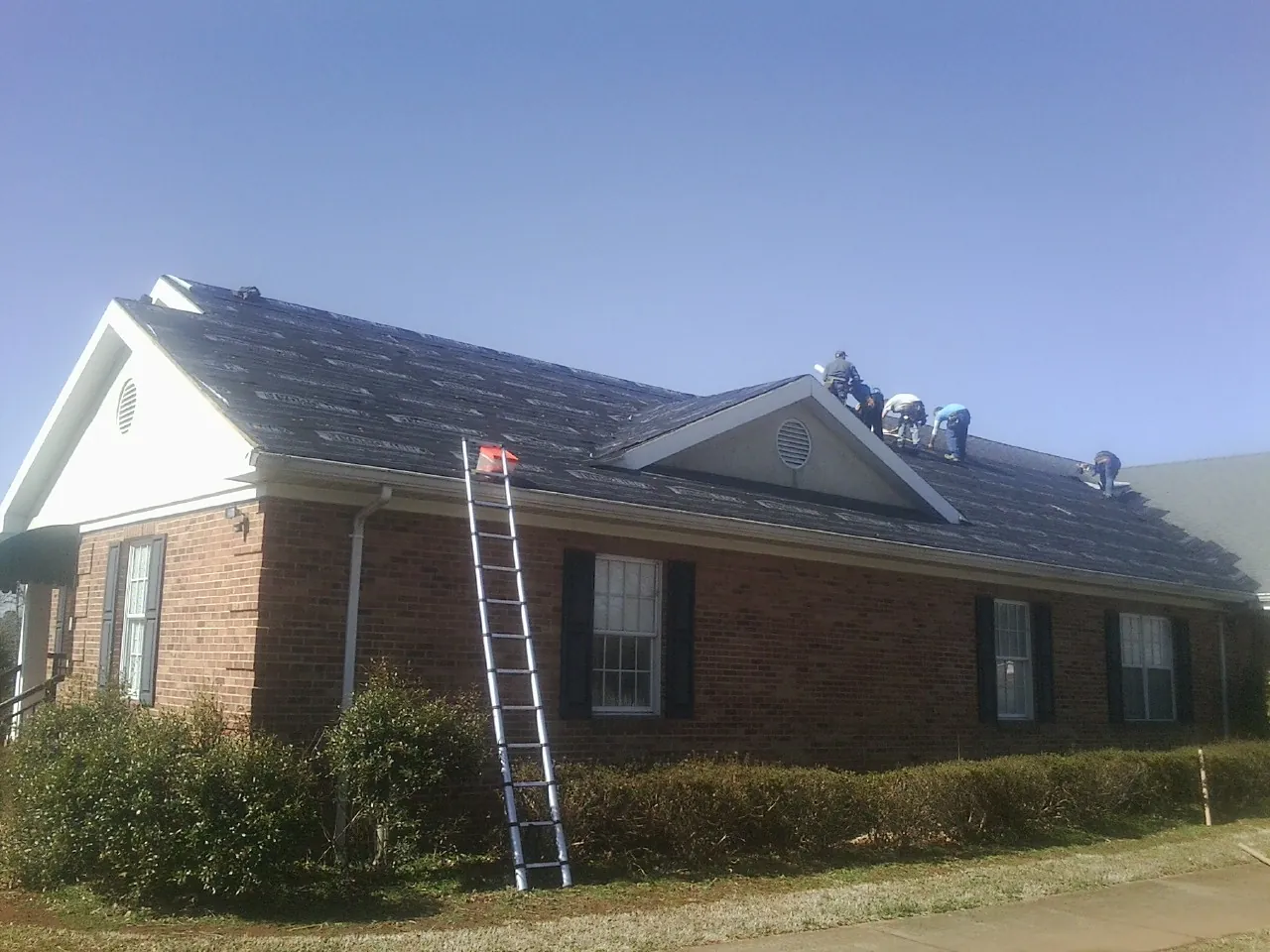 Crew tearing shingles off a brick ranch roof with a ladder set — Emergency Roof Repair work by our crew in Roebling