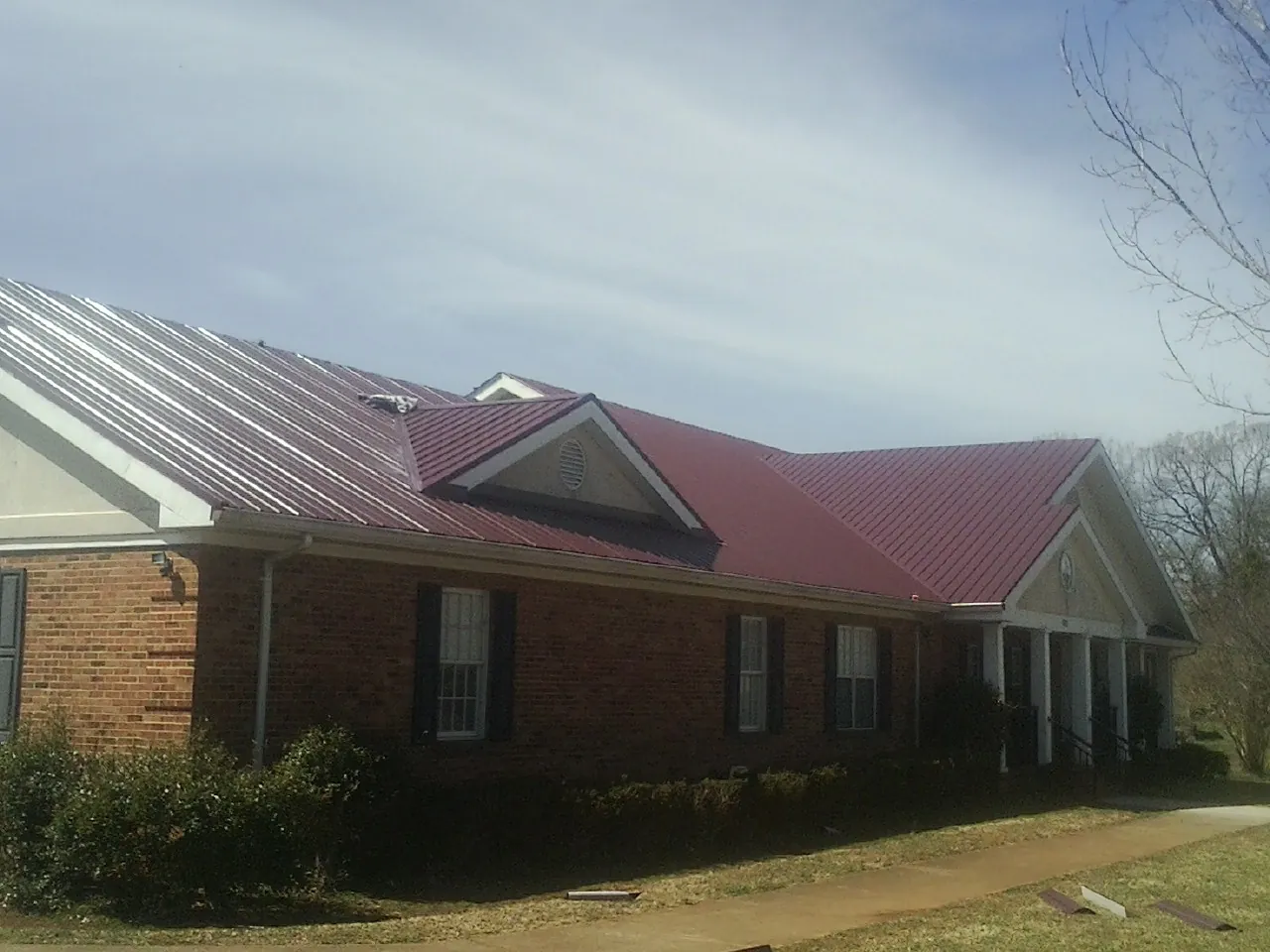 Red metal roof with gabled entries on a long brick building, from a Hail Damage Roof Repair job in Roebling
