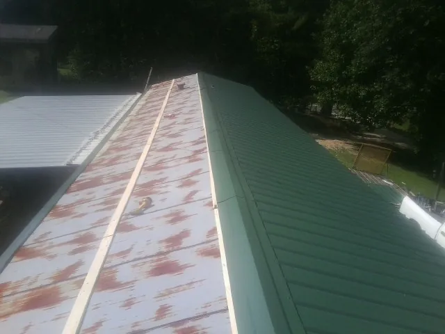 Old rusted panels beside newly installed green metal roofing — Wind Damage Roof Repair by Roofing Brothers in Roebling