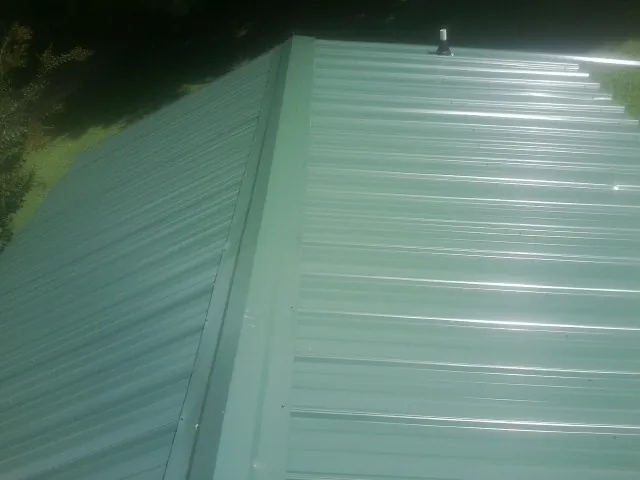 New green metal panels meeting at the ridge of a roof — Flat Roof Repair work by our crew in Roebling