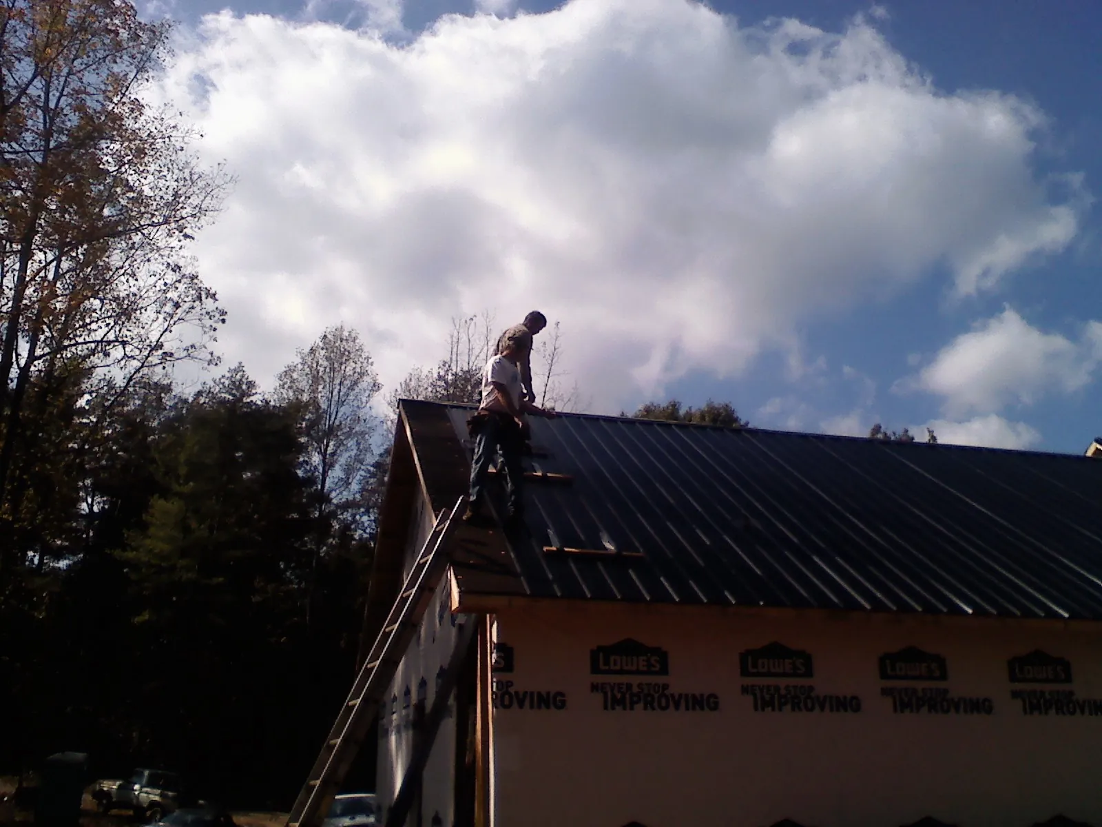 Roofer fastening dark metal panels high against a cloudy sky, from a Roof Inspection job in Roebling