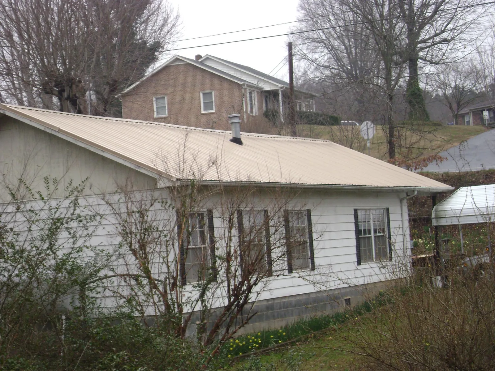 Tan metal roof on a white sided house set into a hillside — Commercial Roofing by Roofing Brothers in Roebling